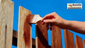 person putting stain paint on wooden fence
