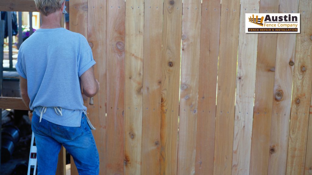 person installing wooden plank on fence
