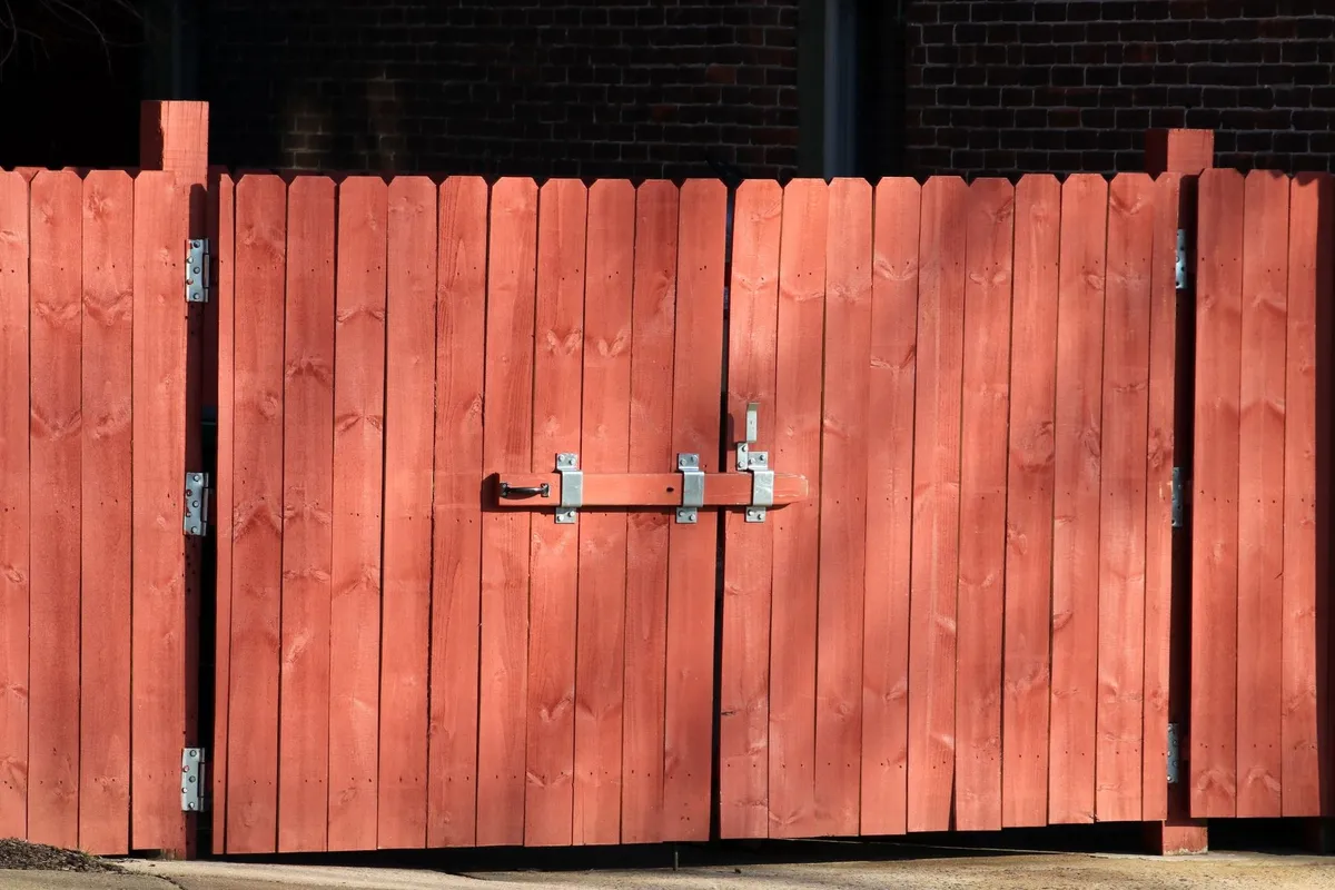 A rustic red wooden fence with a metal latch, highlighting the importance of proper fence maintenance.