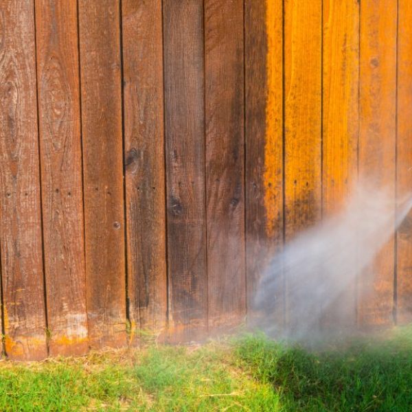 person pressure washing wooden fence